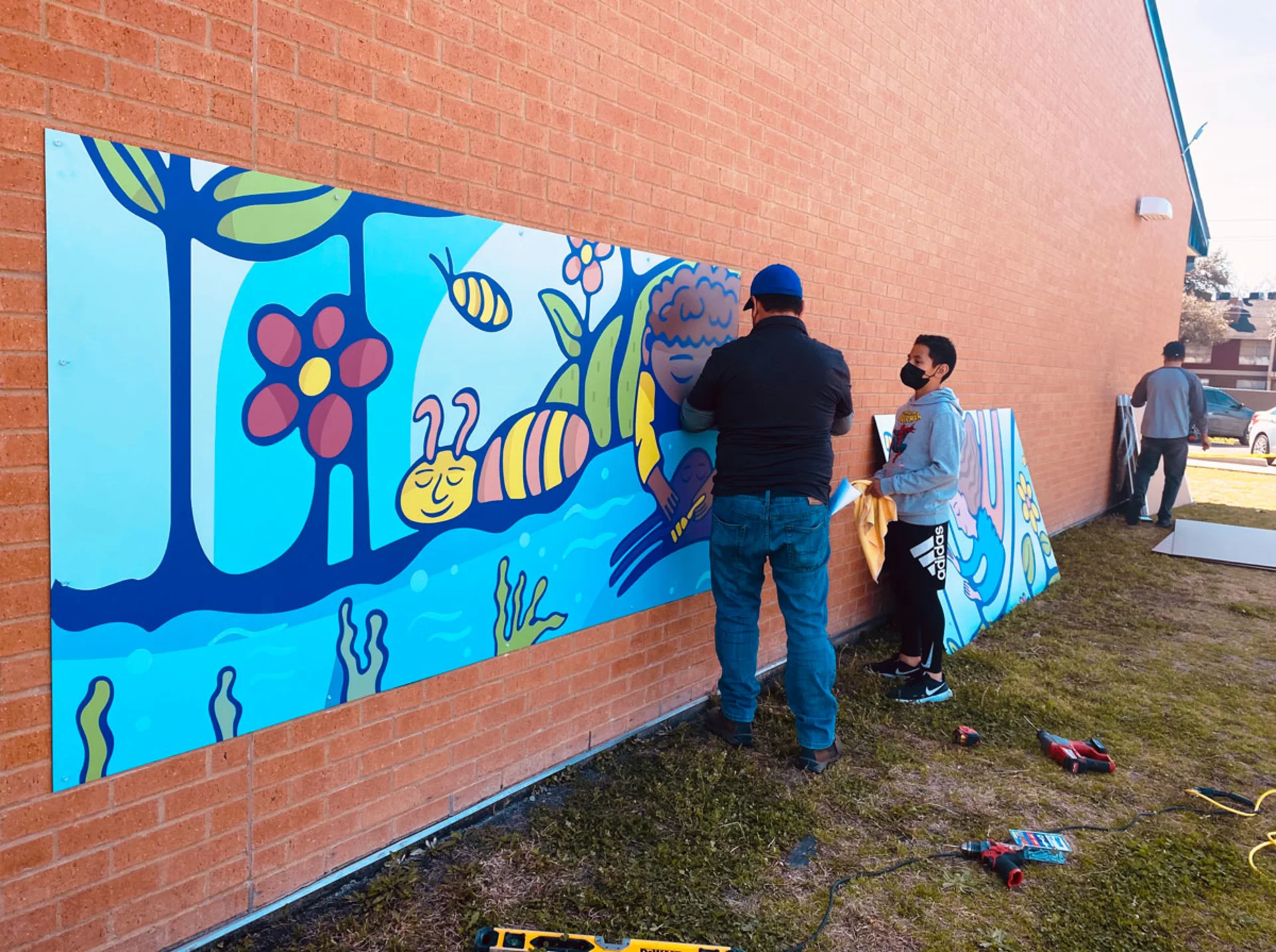 Thomas Printworks crew members install segments of the mural piece by piece along the brick exterior of Burnet Elementary School.