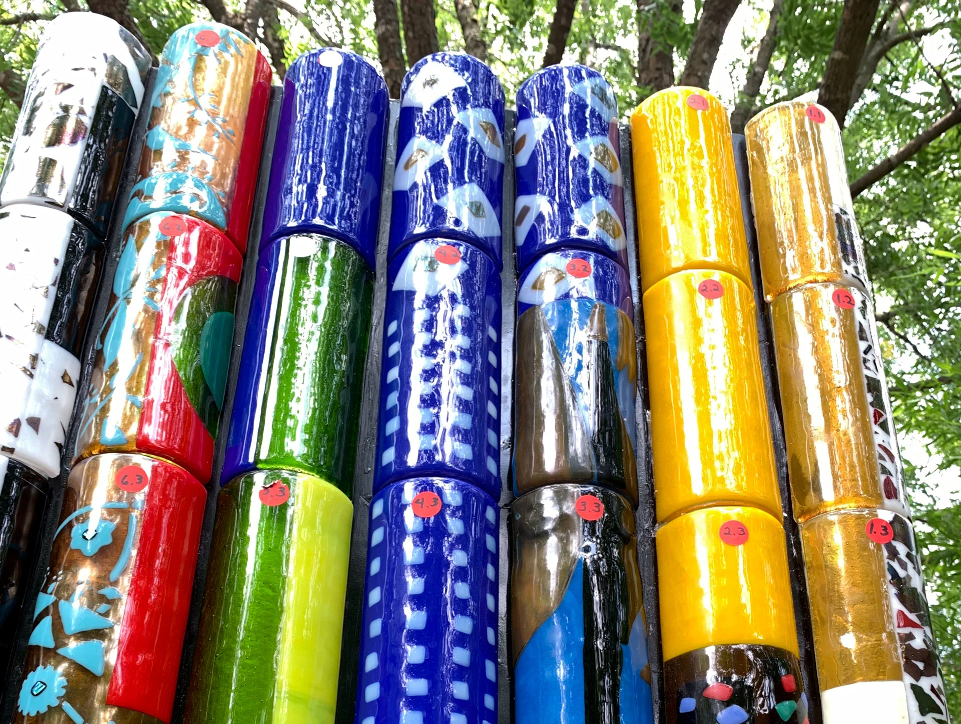 View of the top of Piece 10, which is made of bright red, blue, yellow and green patterned glass cylinders that glint in the sun.