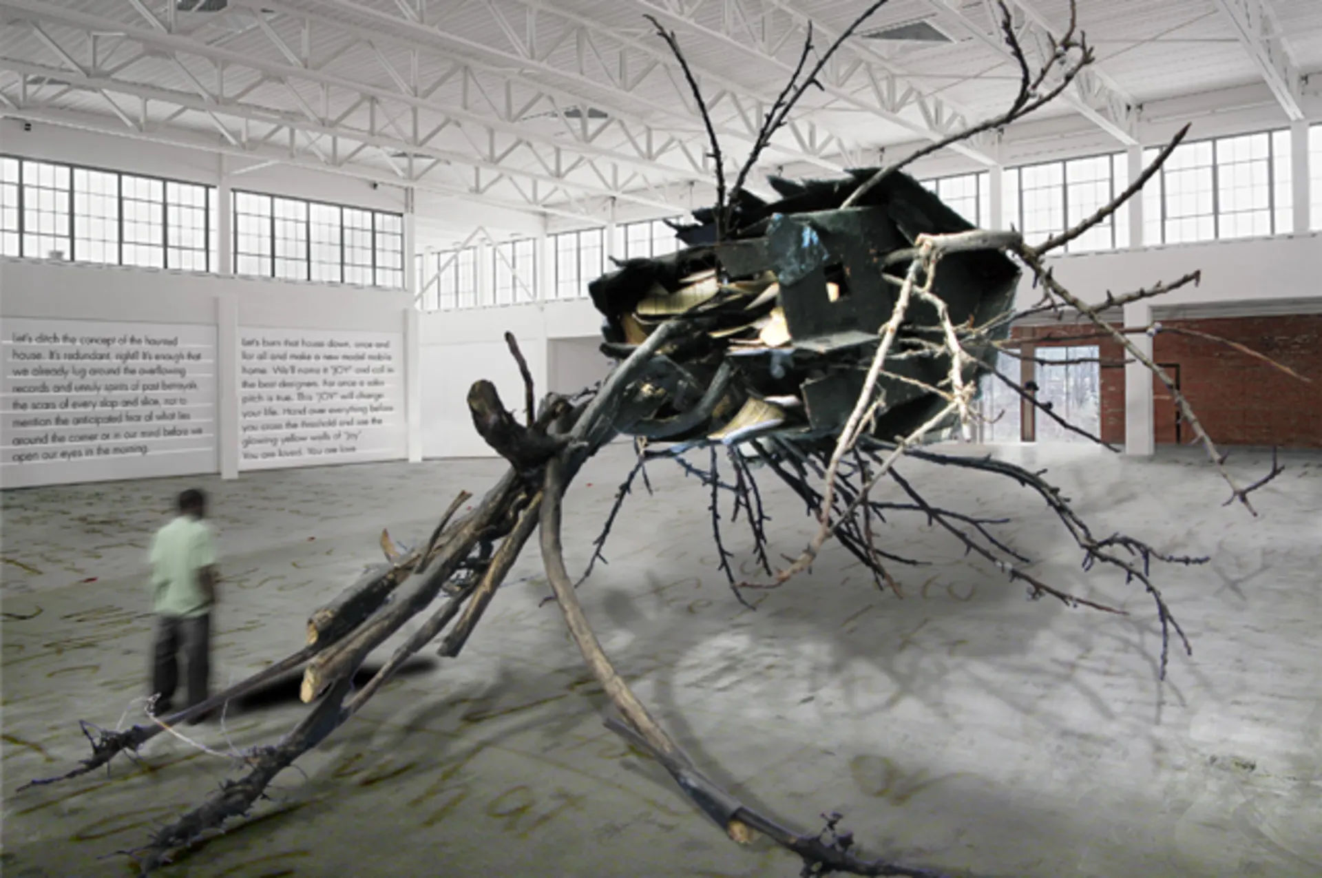 A giant abstract sculpture made of twigs in an industrial warehouse with a message about joy written on the wall and a blurred figure in the background.