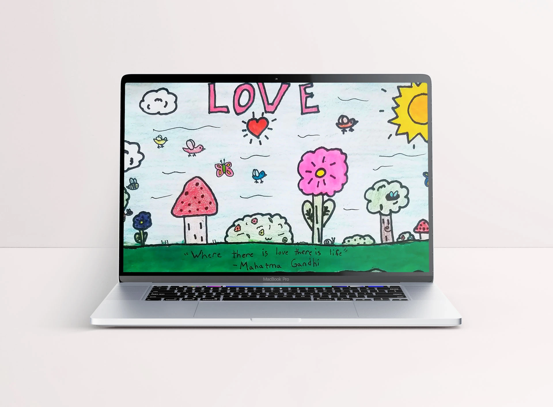 Laptop wallpaper mockup featuring a childlike drawing of a nature scene with birds, insects, trees, flowers and mushrooms along with the word 'Love' and a quote by Mahatma Gandhi.