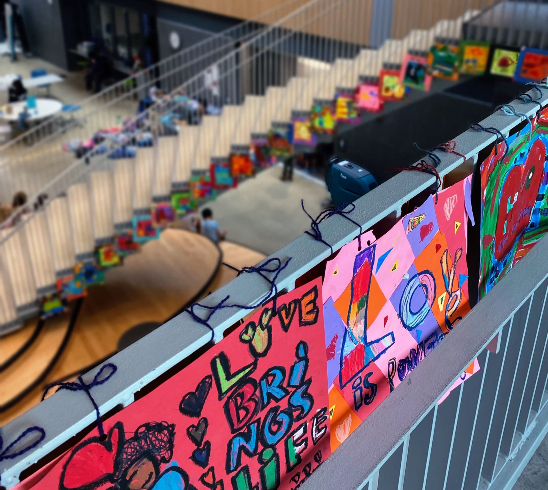 A bird’s-eye view of a large rounded staircase in Maury Elementary School lined with dozens of colorful square drawings attached to the railing with string.