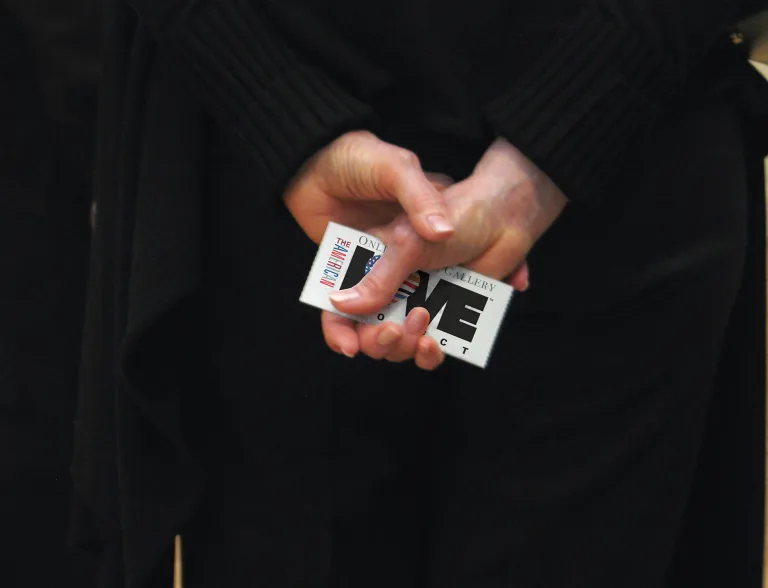 Hands clasped behind a person's back holding a ticket with the American Love Project logo and the text 'Online gallery'.