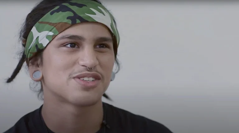 Close up of Richard Rodriguez, a high school student, wearing a camouflage bandana, gauge earrings, and sitting in front of a white backdrop.