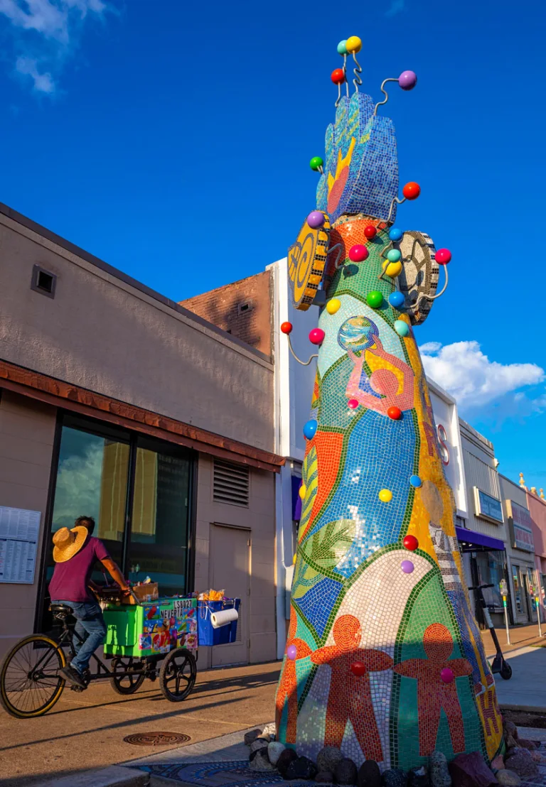 The bright, colorful Piece 24 glints in the sun as a man on a bike passes by.