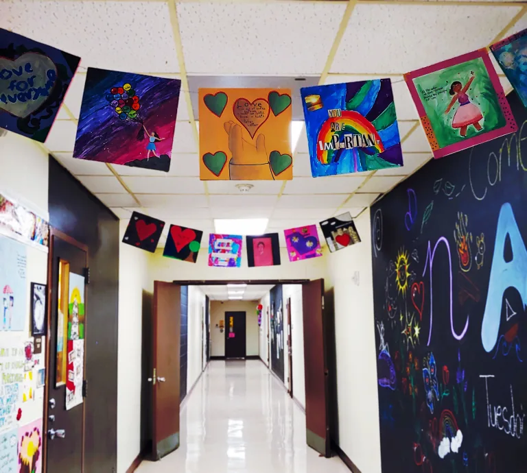Paper flag garlands featuring square pieces of student artwork decorate the ceiling of a school hallway.