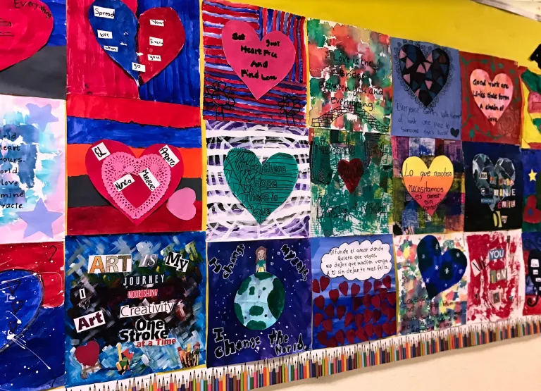 Colorful school bulletin board displaying student artwork with hearts, messages about love in Spanish and English, and collages.