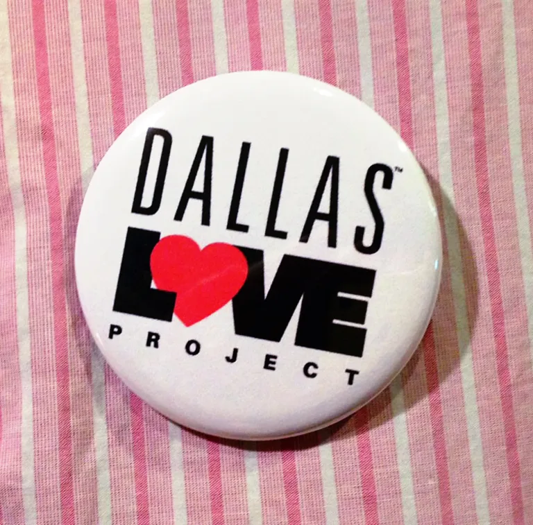 A pin with the Dallas Love Project logo featuring a red heart rests on a striped pink tablecloth