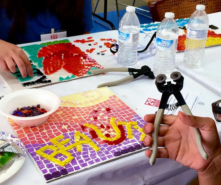 Close up of table strewn with art supplies, tools, mosaic art and tiles.