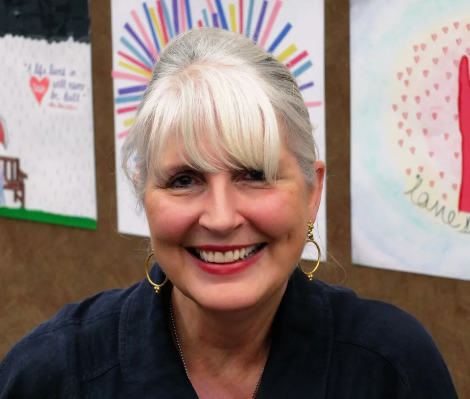 Blessen smiling in front of a bulletin board with student artwork.