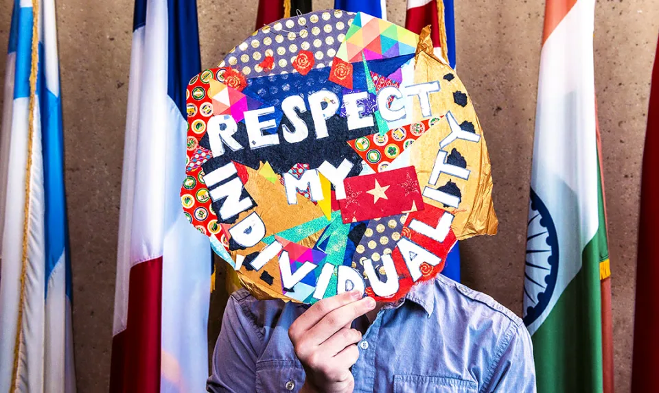 A 29 Pieces student intern holds up a circular piece of art with a collage of colors and patterns along with the text, 'Respect my individuality'.