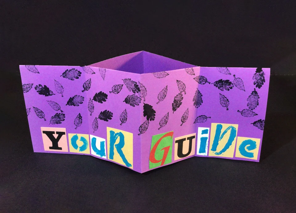 A purple zine with stamped images of leaves, halfway folded to reveal the words "Your Guide" in cutout letters.