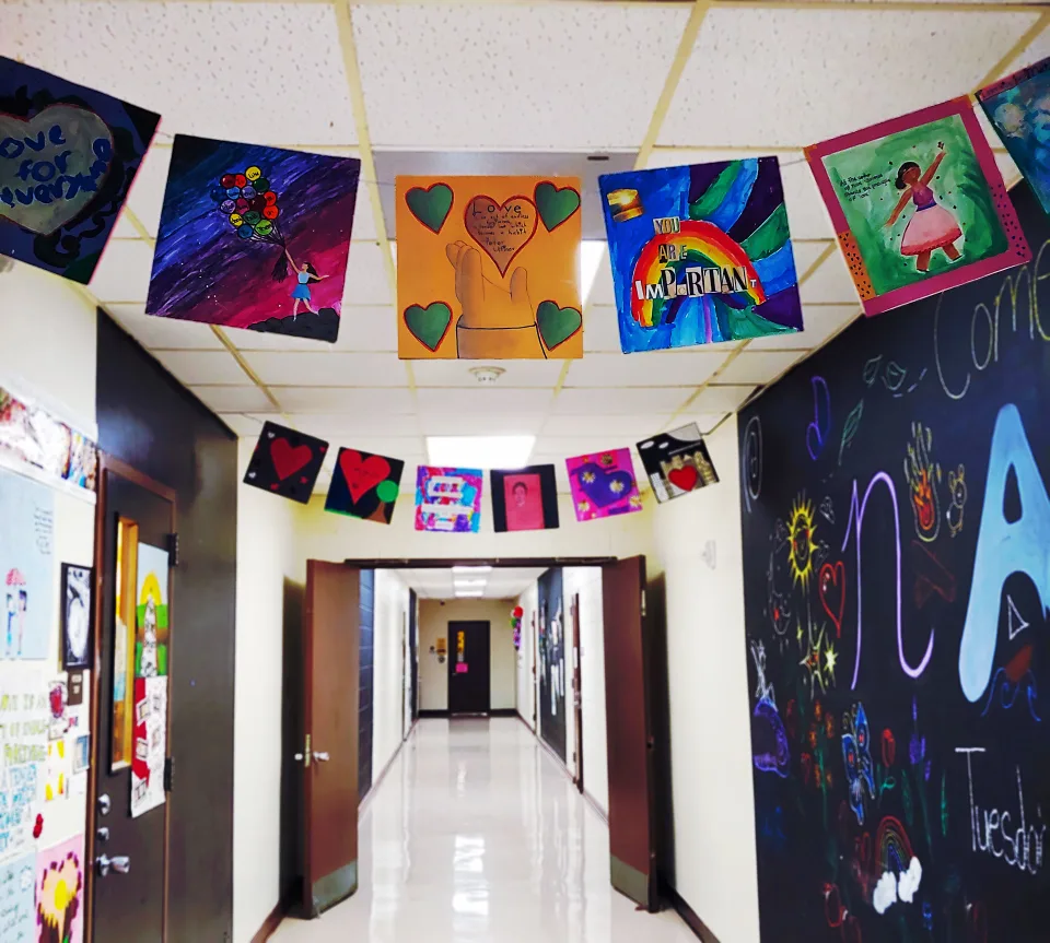 Paper flag garlands featuring square pieces of student artwork decorate the ceiling of a school hallway.