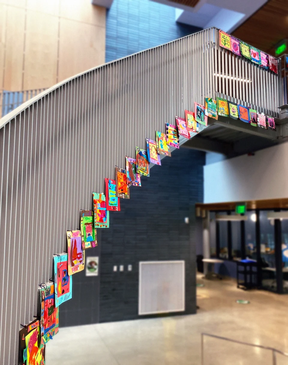 A view from the ground of another staircase in Maury Elementary School lined with dozens of colorful square drawings.