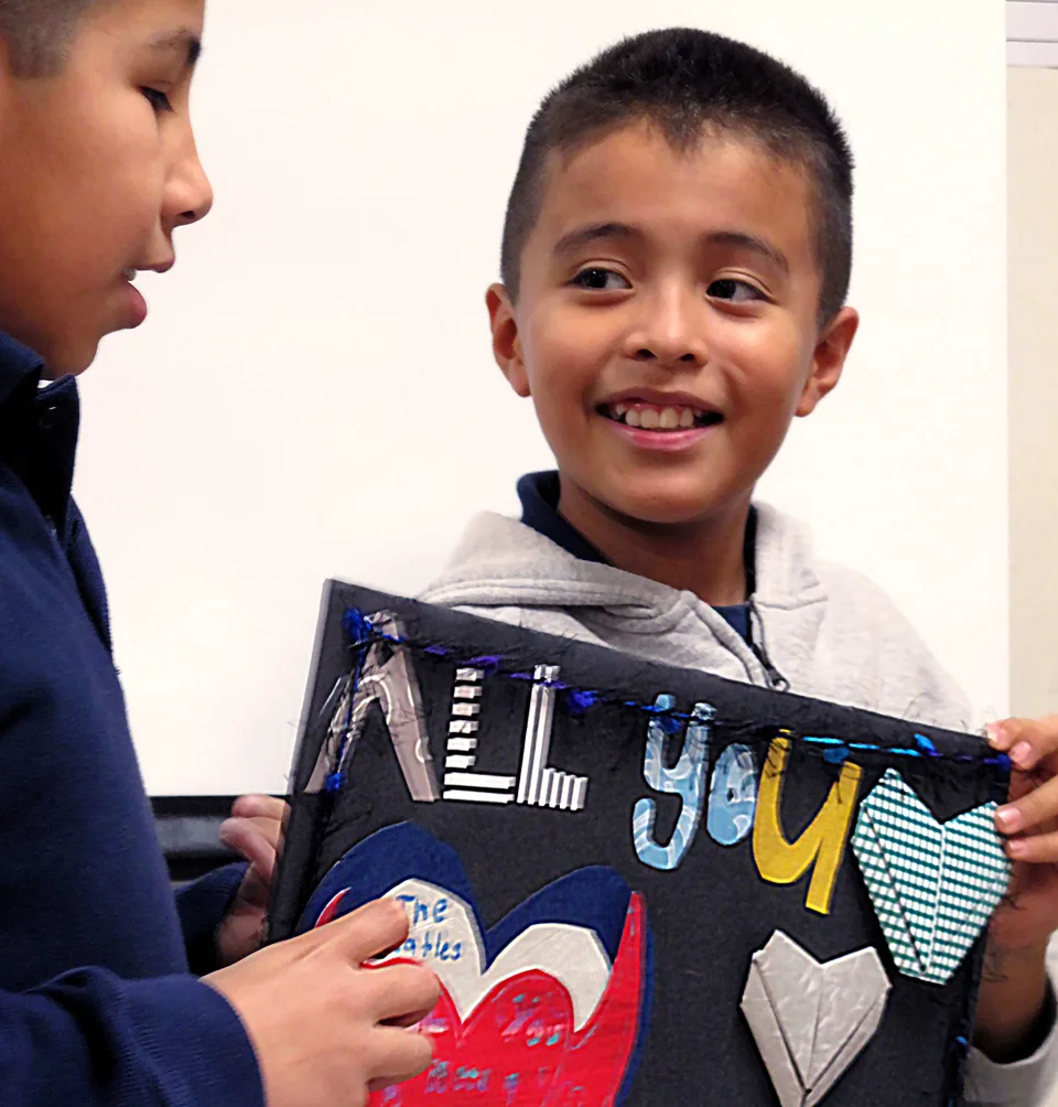 Two young boys hold a piece of artwork featuring a quote by The Beatles.
