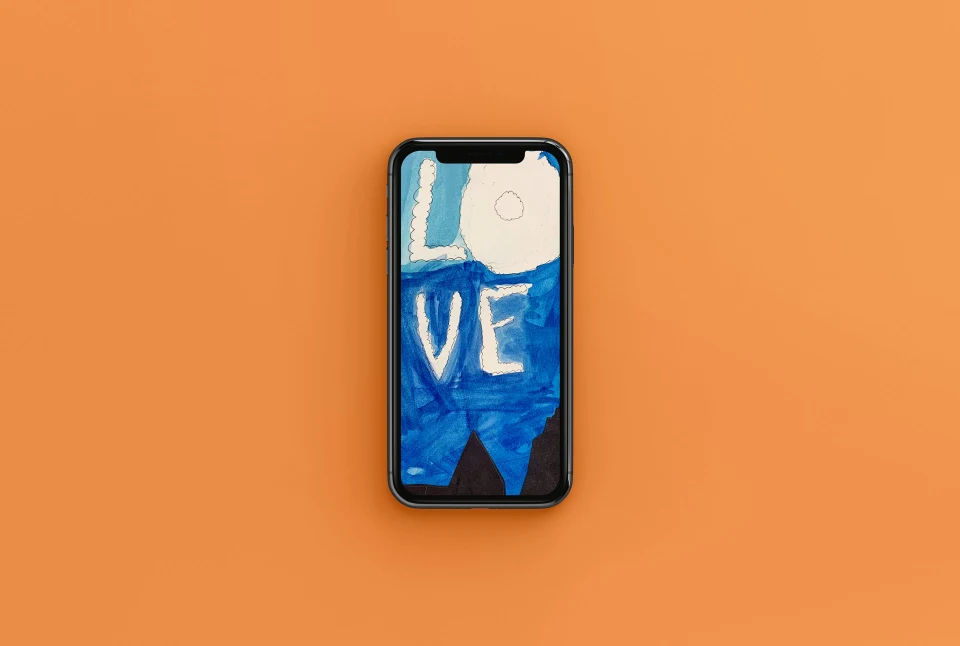 An aerial view of an iPhone, whose wallpaper is a piece of blue watercolor art containing the word 'love', set against an orange background.